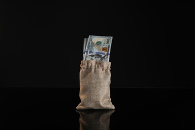 Photo of Dollar banknotes in burlap sack on dark mirror surface