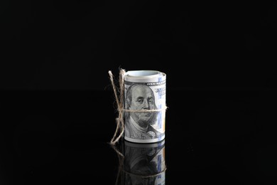 Photo of Rolled dollar banknotes with rope on dark mirror surface