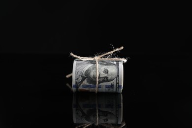 Photo of Rolled dollar banknotes with rope on dark mirror surface