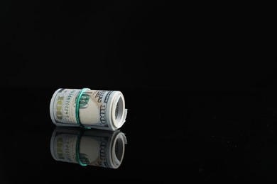 Photo of Rolled dollar banknotes with rubber band on dark mirror surface, space for text