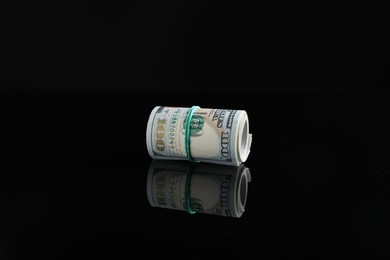 Photo of Rolled dollar banknotes with rubber band on dark mirror surface