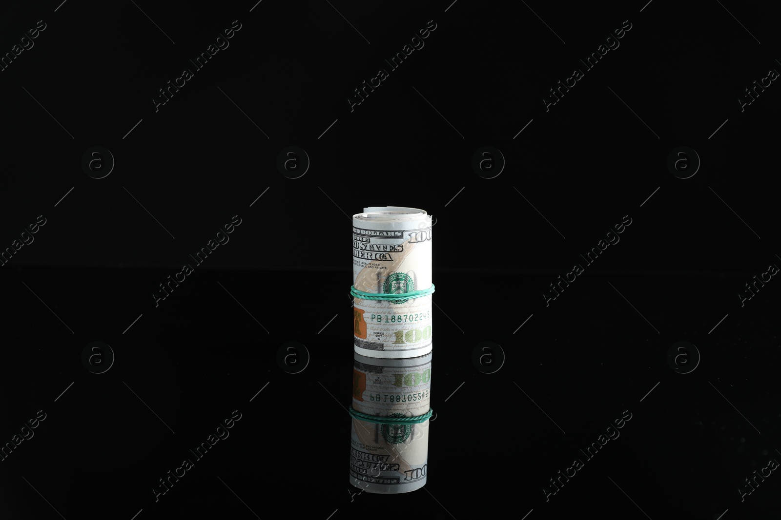 Photo of Rolled dollar banknotes with rubber band on dark mirror surface