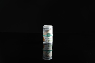 Photo of Rolled dollar banknotes with rubber band on dark mirror surface