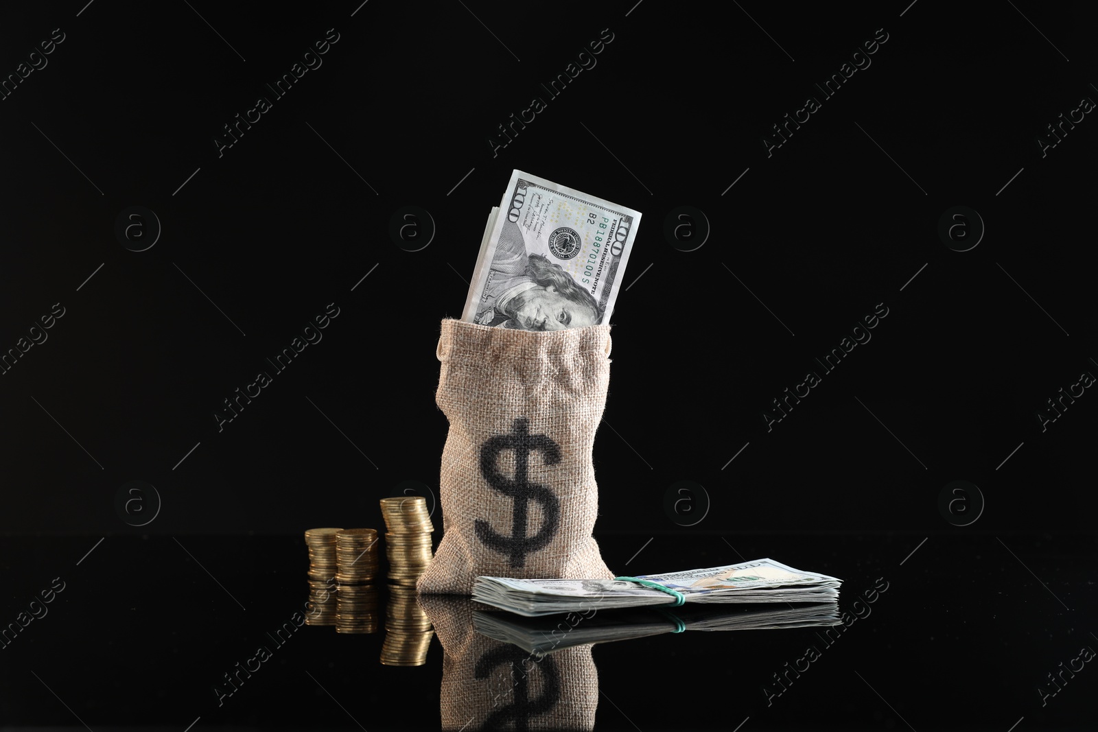 Photo of Burlap sack with dollar banknotes and stacked coins on dark mirror surface