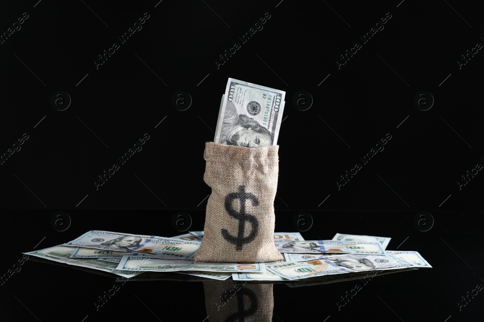 Photo of Burlap sack with dollar banknotes on dark mirror surface