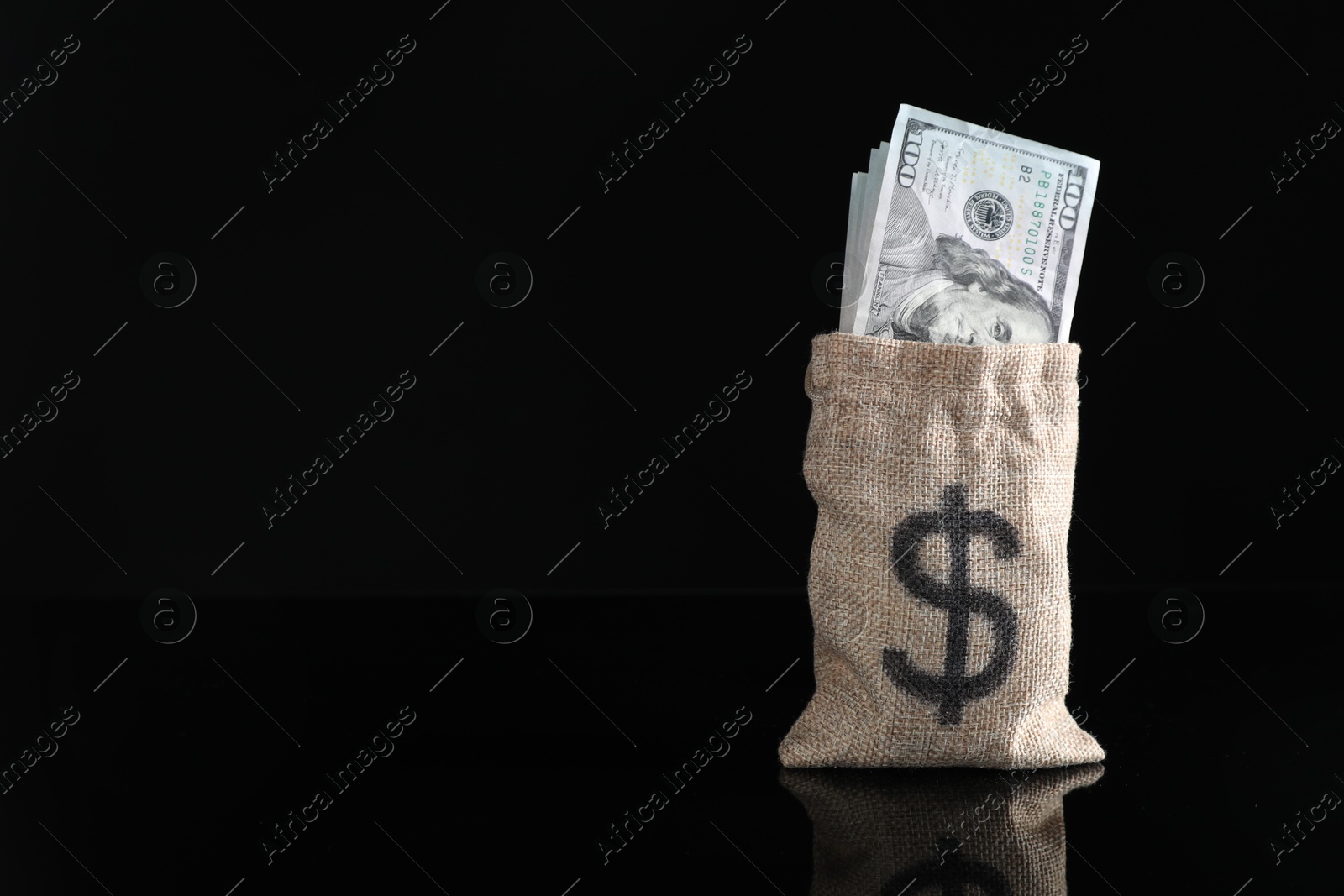 Photo of Dollar banknotes in burlap sack on dark mirror surface, space for text