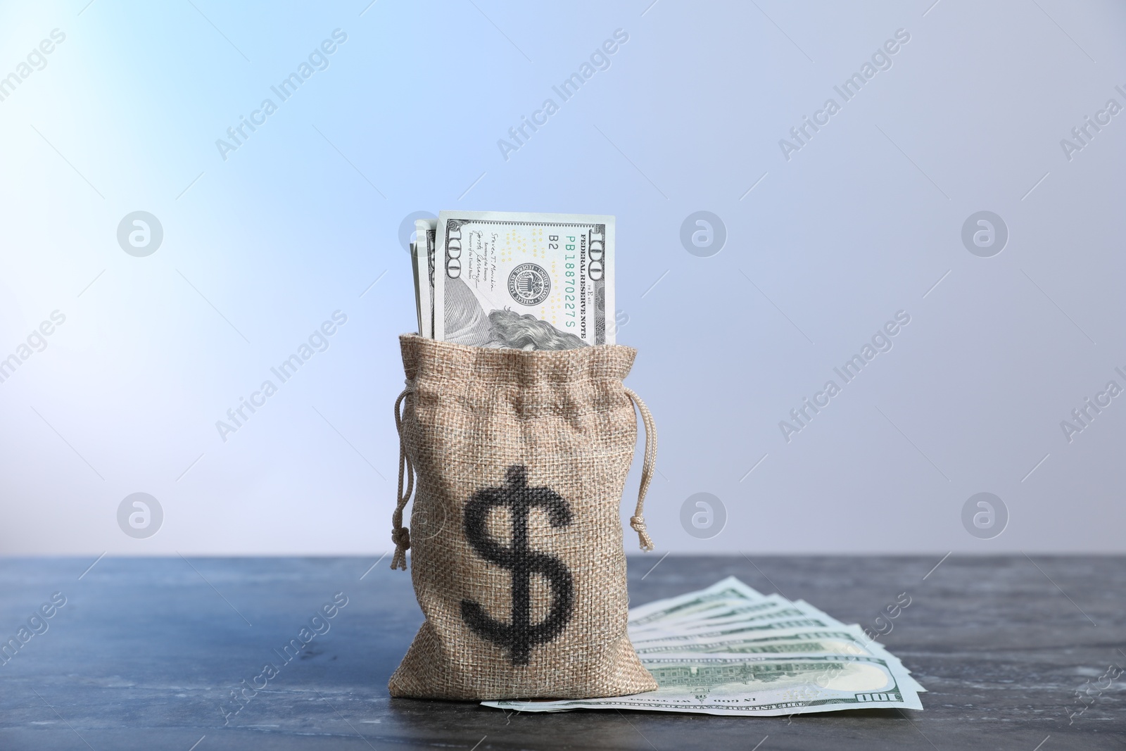 Photo of Burlap sack with dollar banknotes on grey table