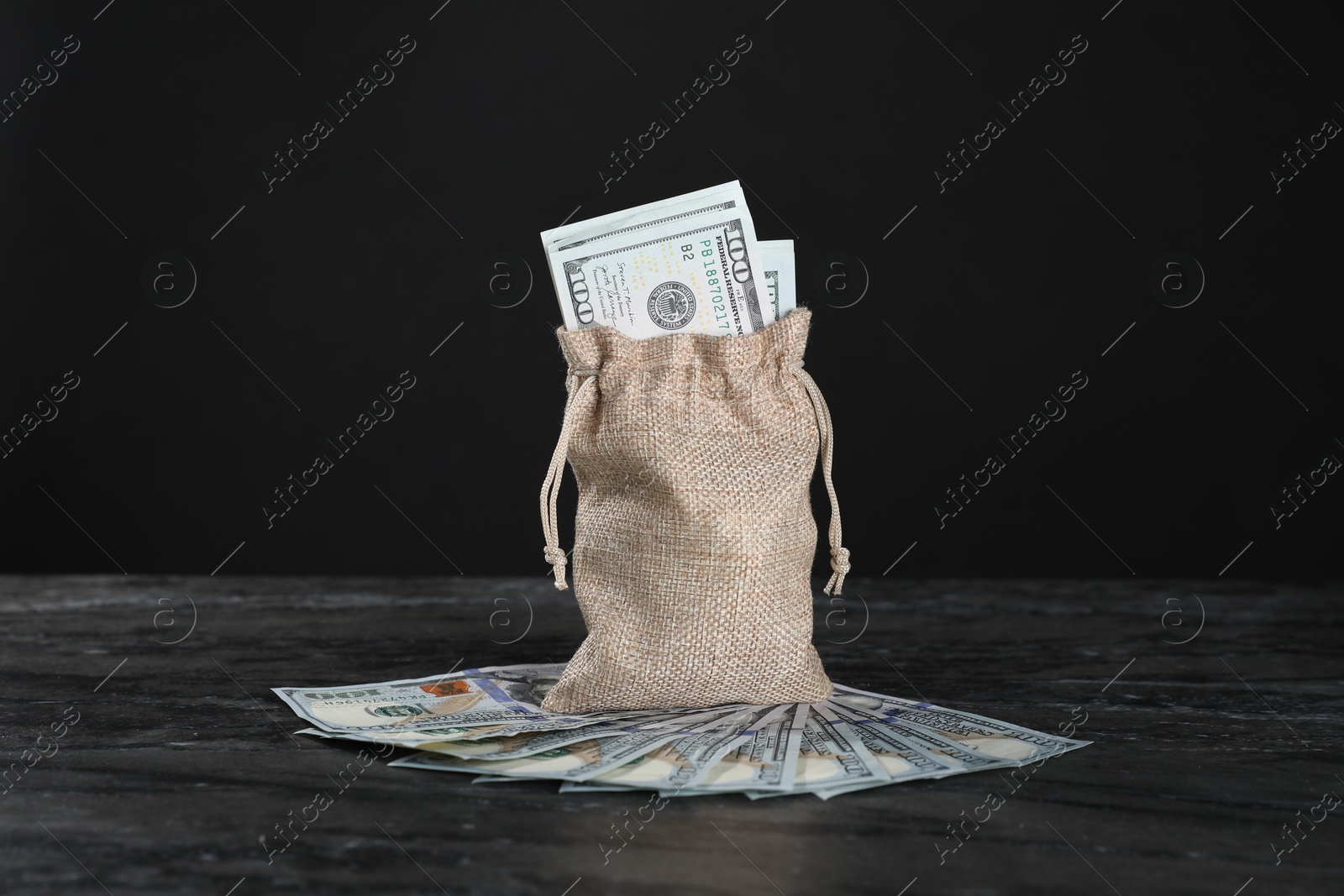 Photo of Burlap sack with dollar banknotes on grey table