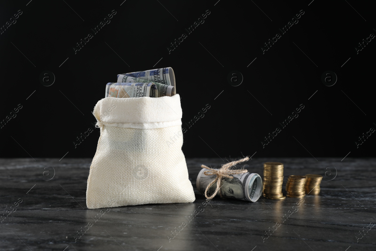 Photo of Burlap sack with dollar banknotes and stacked coins on grey table