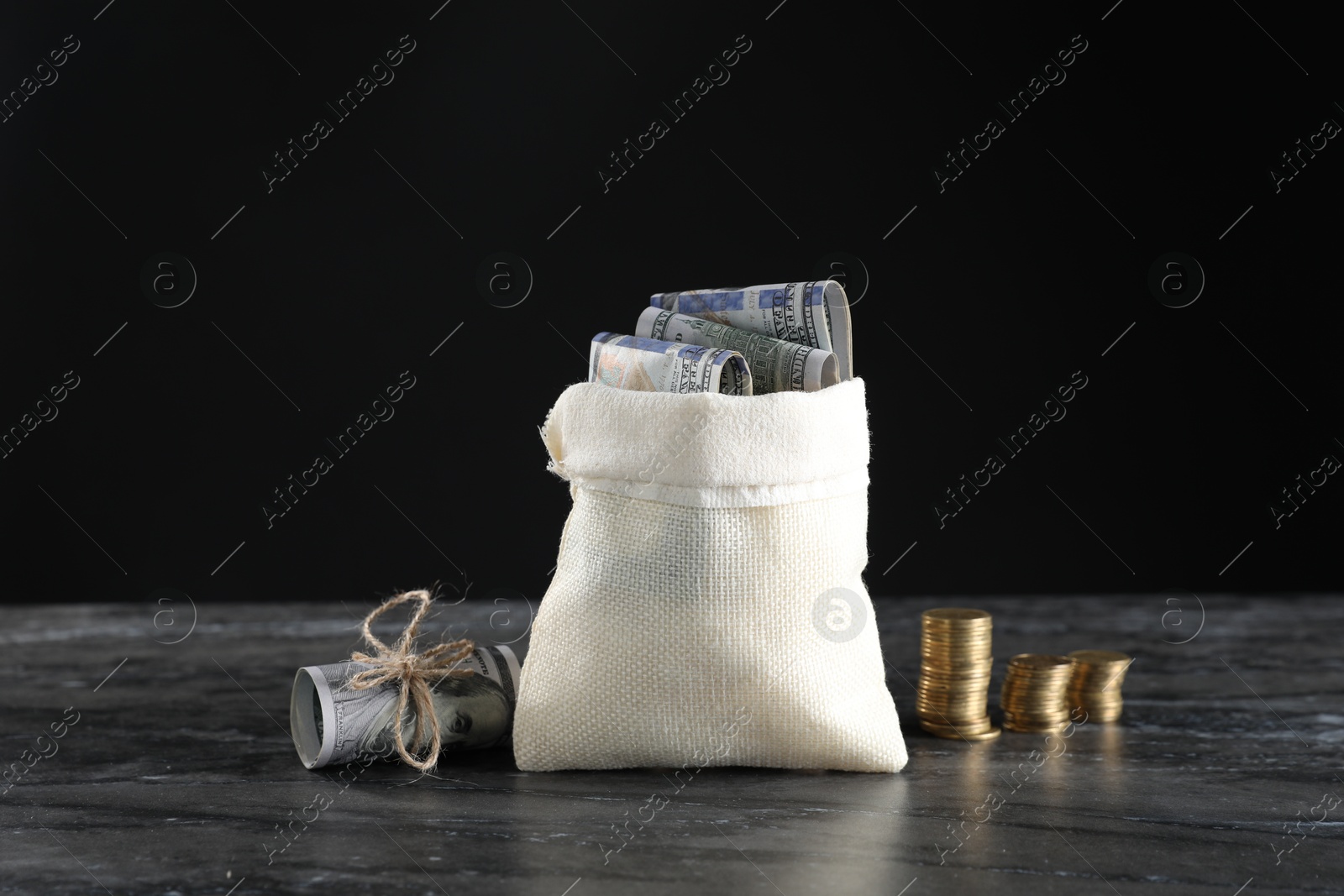 Photo of Burlap sack with dollar banknotes and stacked coins on grey table