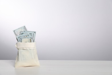 Photo of Dollar banknotes in burlap sack on white table, space for text