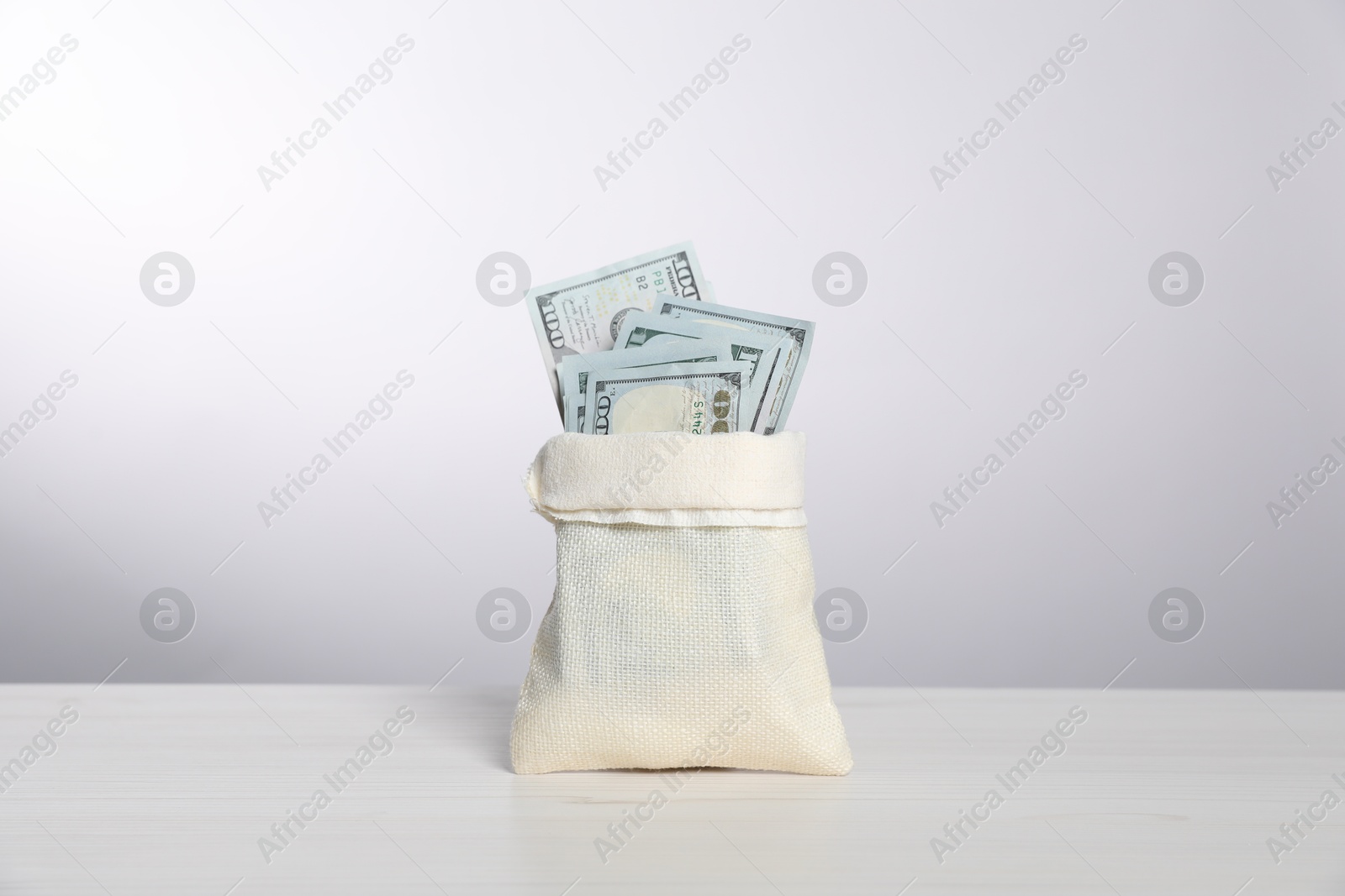 Photo of Dollar banknotes in burlap sack on white table