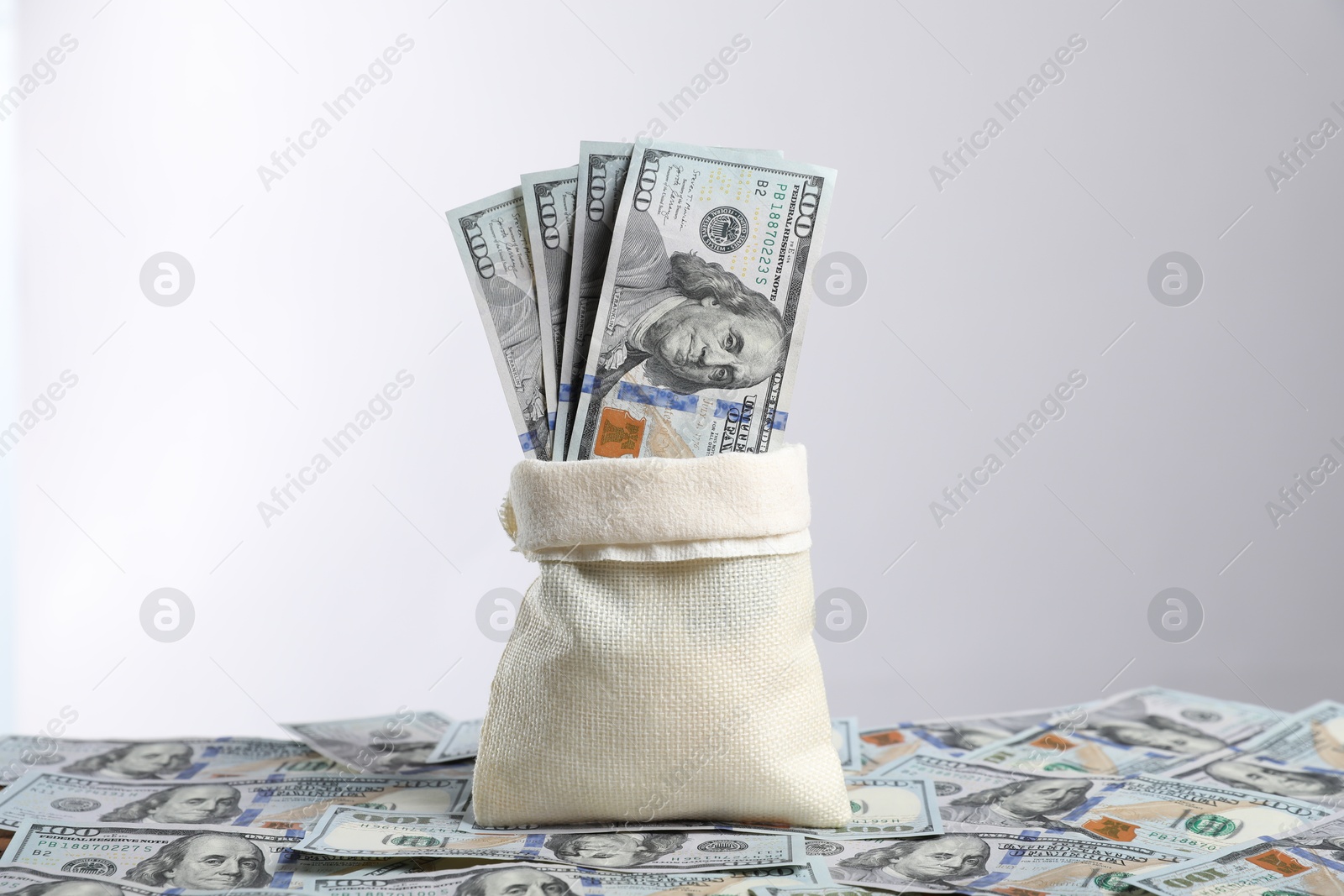 Photo of Burlap sack with dollar banknotes against light background