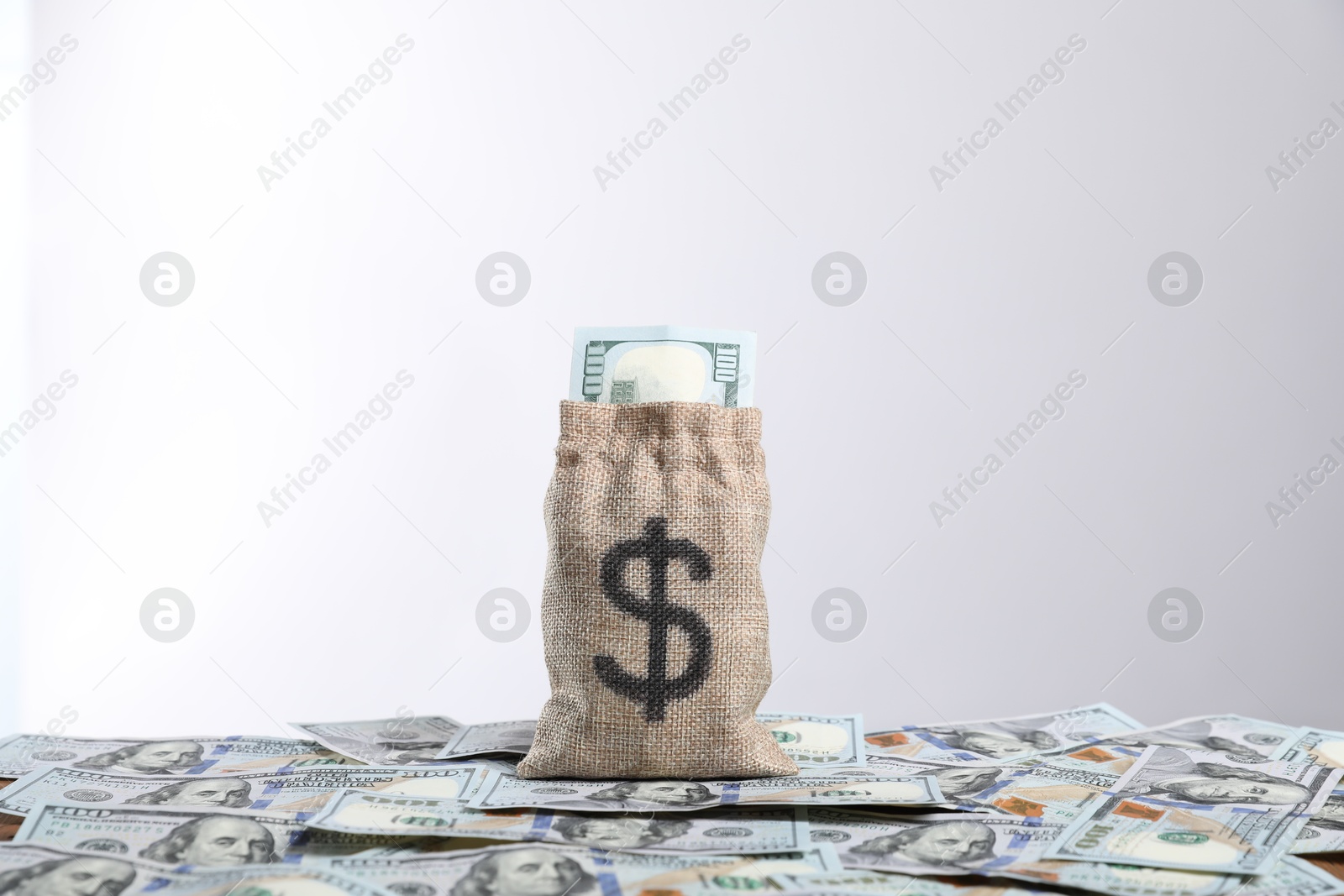 Photo of Burlap sack with dollar banknotes against light background