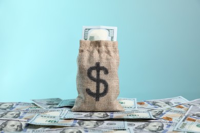 Photo of Burlap sack with dollar banknotes against light blue background