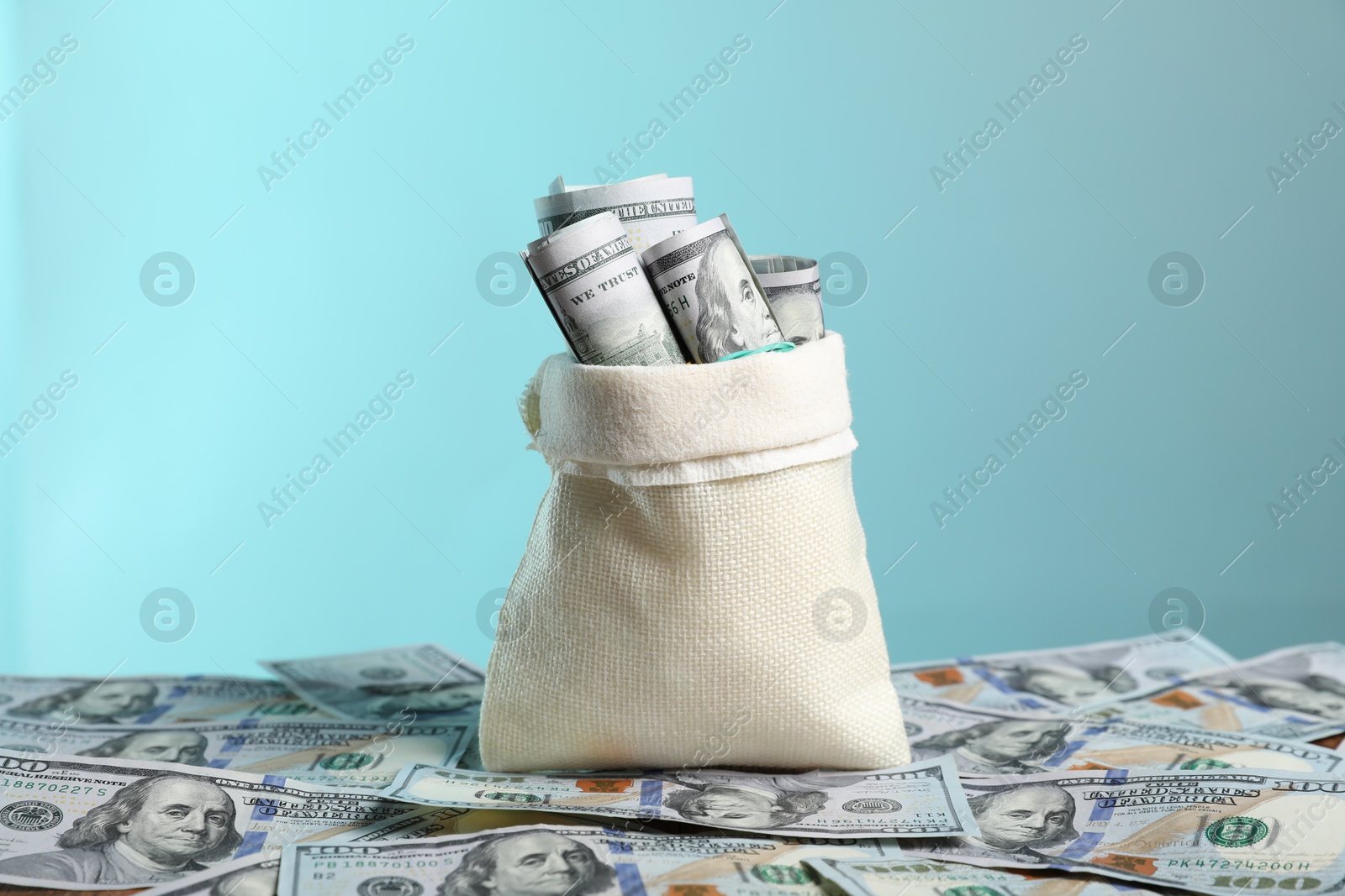 Photo of Burlap sack with dollar banknotes against light blue background