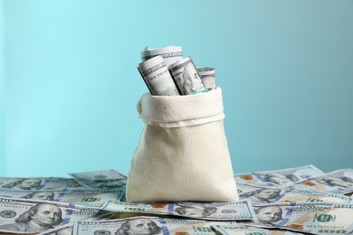 Photo of Burlap sack with dollar banknotes against light blue background