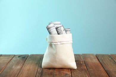 Photo of Dollar banknotes in burlap sack on wooden table against light blue background