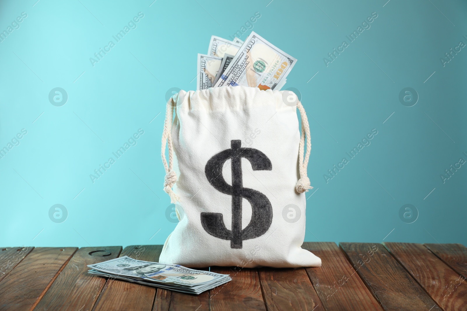 Photo of Burlap sack with dollar banknotes on wooden table against light blue background