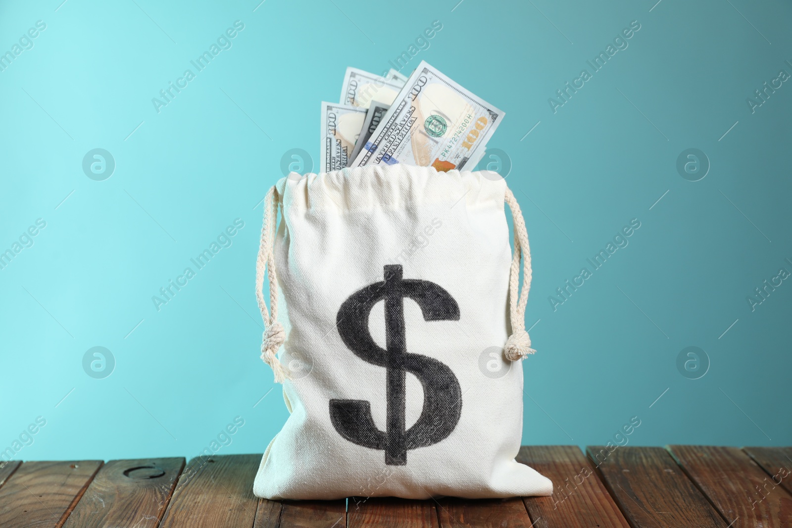 Photo of Dollar banknotes in burlap sack on wooden table against light blue background