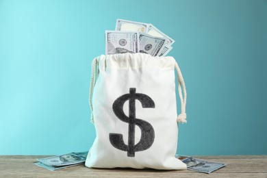 Photo of Burlap sack with dollar banknotes on wooden table against light blue background