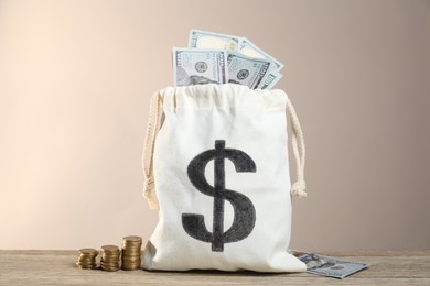 Photo of Burlap sack with dollar banknotes and stacked coins on wooden table against beige background