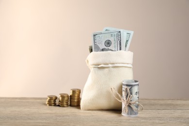 Photo of Burlap sack with dollar banknotes and stacked coins on wooden table against beige background