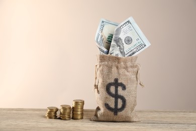 Photo of Burlap sack with dollar banknotes and stacked coins on wooden table against beige background