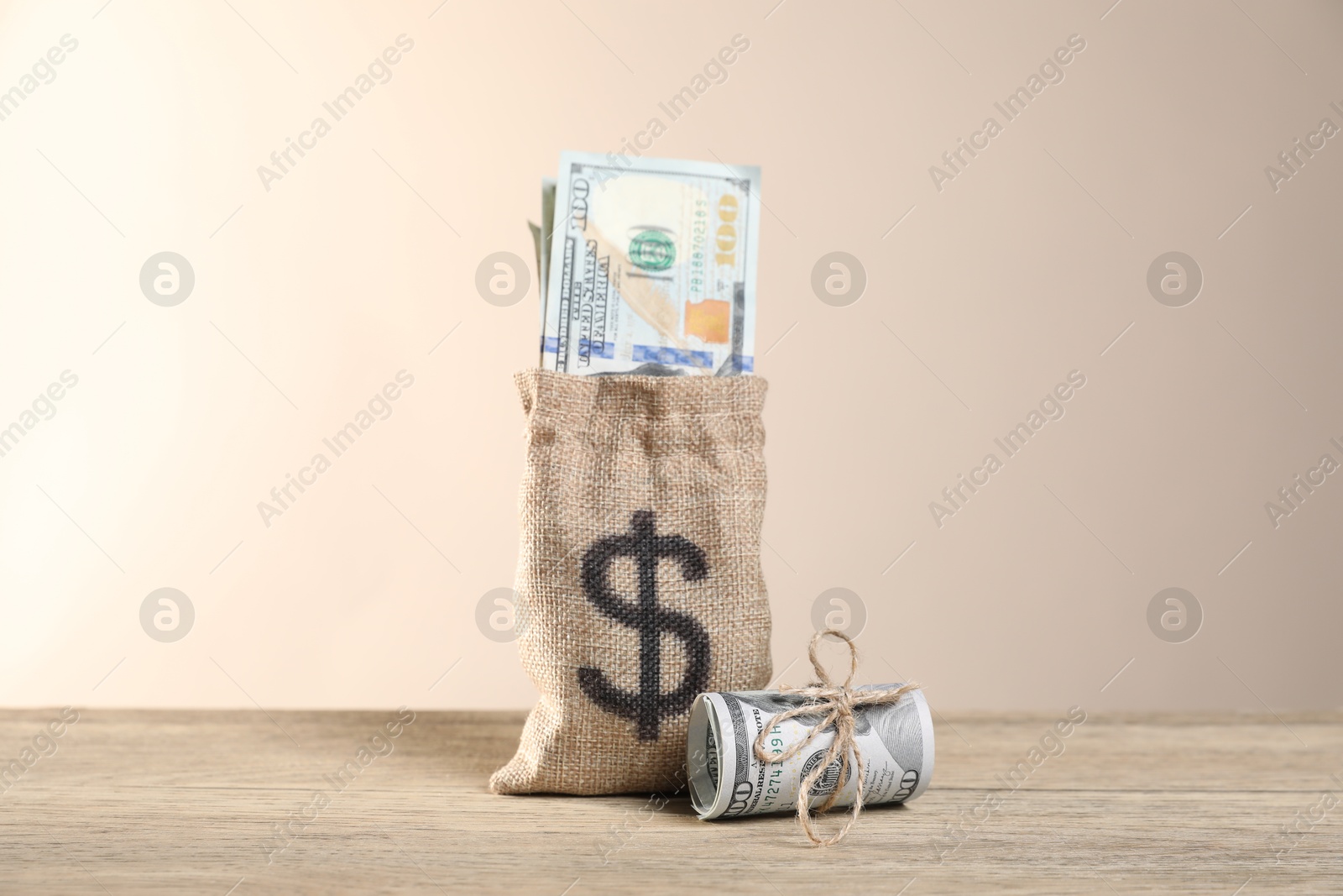 Photo of Burlap sack with dollar banknotes on wooden table against beige background