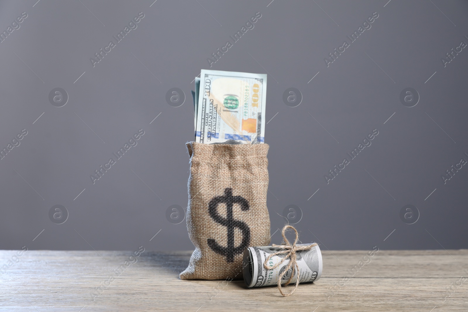 Photo of Burlap sack with dollar banknotes on wooden table against grey background