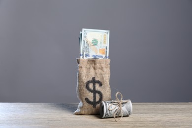 Photo of Burlap sack with dollar banknotes on wooden table against grey background