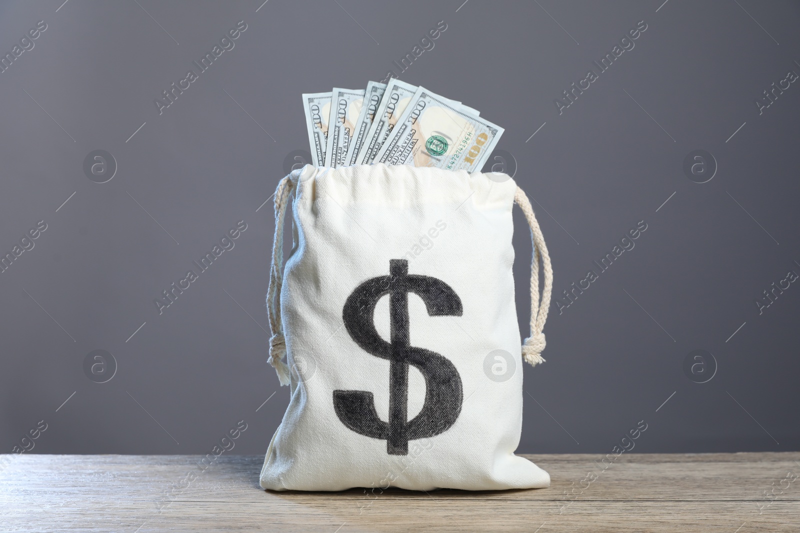 Photo of Dollar banknotes in burlap sack on wooden table against grey background