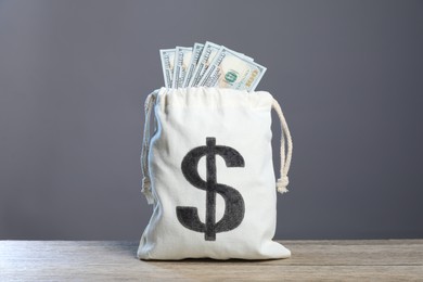 Photo of Dollar banknotes in burlap sack on wooden table against grey background