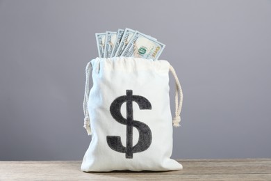 Photo of Dollar banknotes in burlap sack on wooden table against grey background