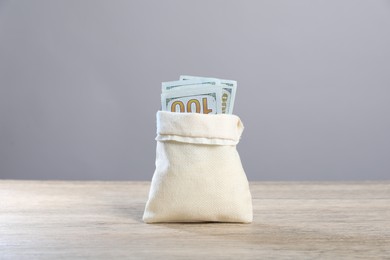 Photo of Dollar banknotes in burlap sack on wooden table against grey background