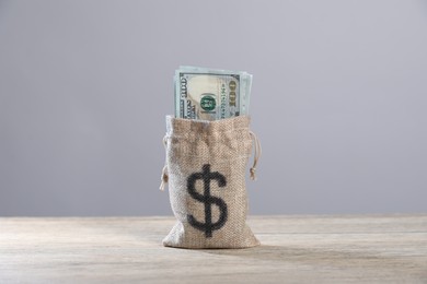 Photo of Dollar banknotes in burlap sack on wooden table against grey background