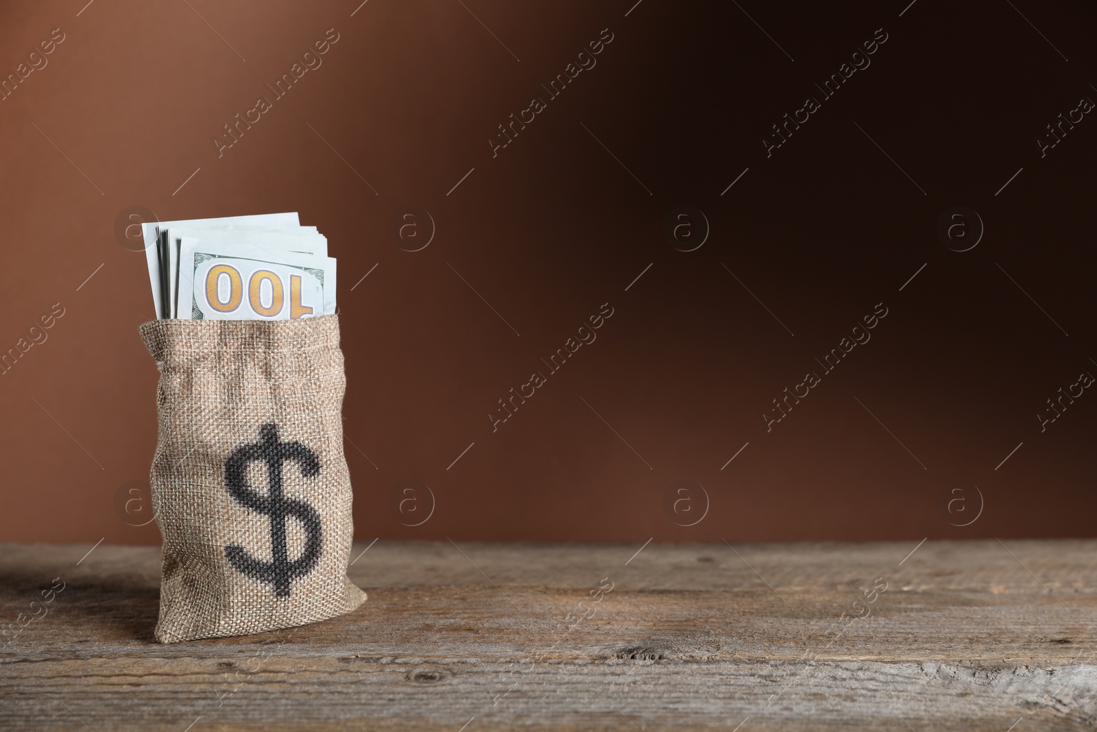 Photo of Dollar banknotes in burlap sack on wooden table against brown background, space for text