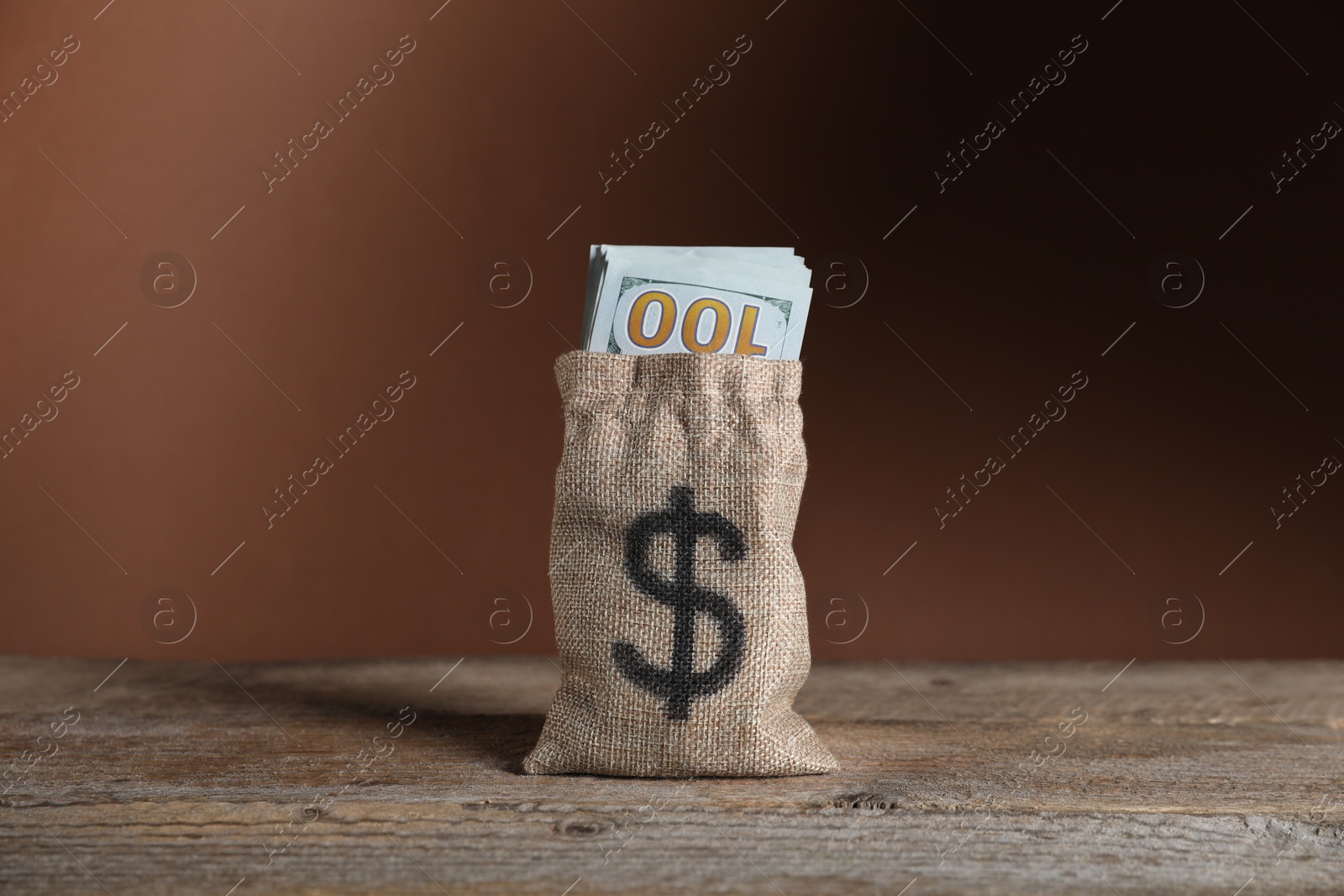 Photo of Dollar banknotes in burlap sack on wooden table against brown background