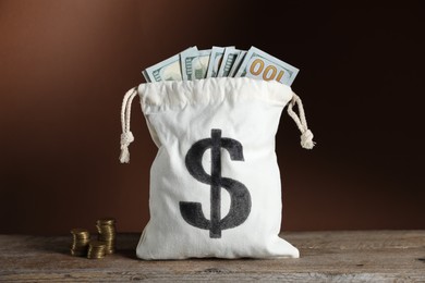 Photo of Dollar banknotes in burlap sack and stacked coins on wooden table against brown background