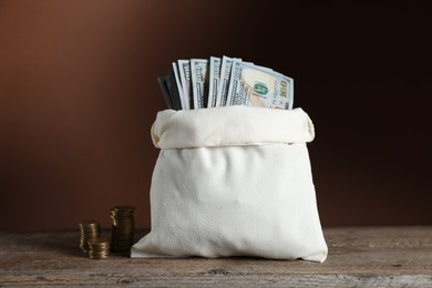 Photo of Dollar banknotes in burlap sack and stacked coins on wooden table against brown background