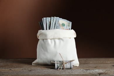 Photo of Burlap sack with dollar banknotes on wooden table against brown background