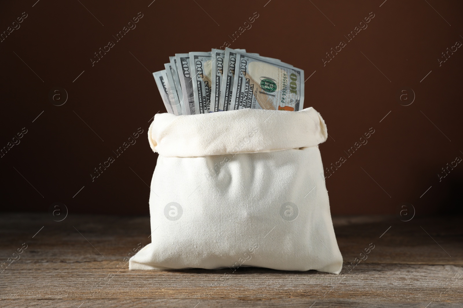 Photo of Dollar banknotes in burlap sack on wooden table against brown background