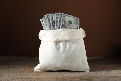 Photo of Dollar banknotes in burlap sack on wooden table against brown background