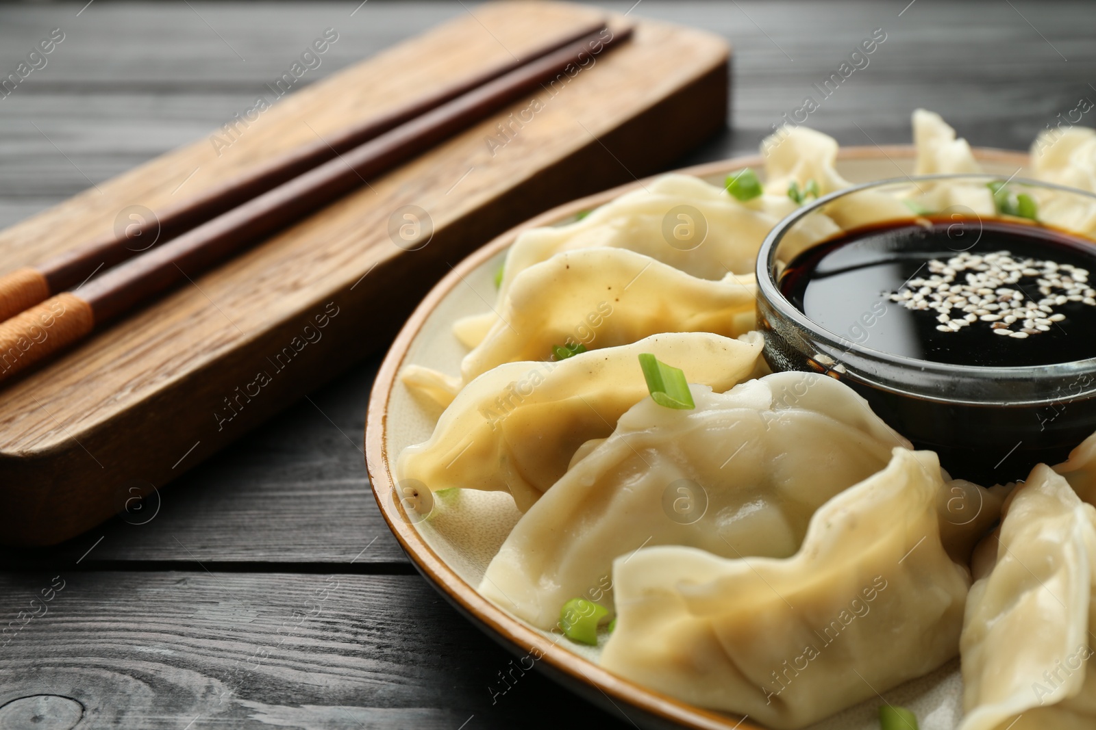 Photo of Tasty boiled gyoza (dumplings) with green onion served on black wooden table, closeup