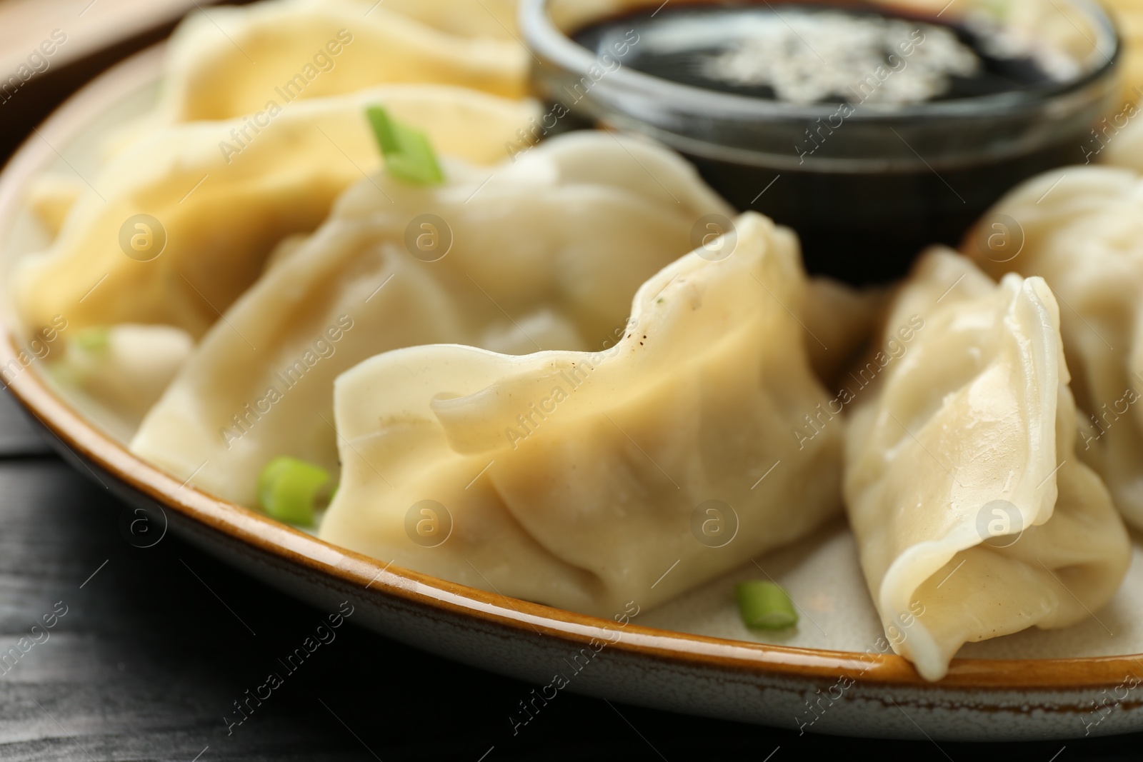 Photo of Tasty boiled gyoza (dumplings) with green onion and soy sauce on black table, closeup