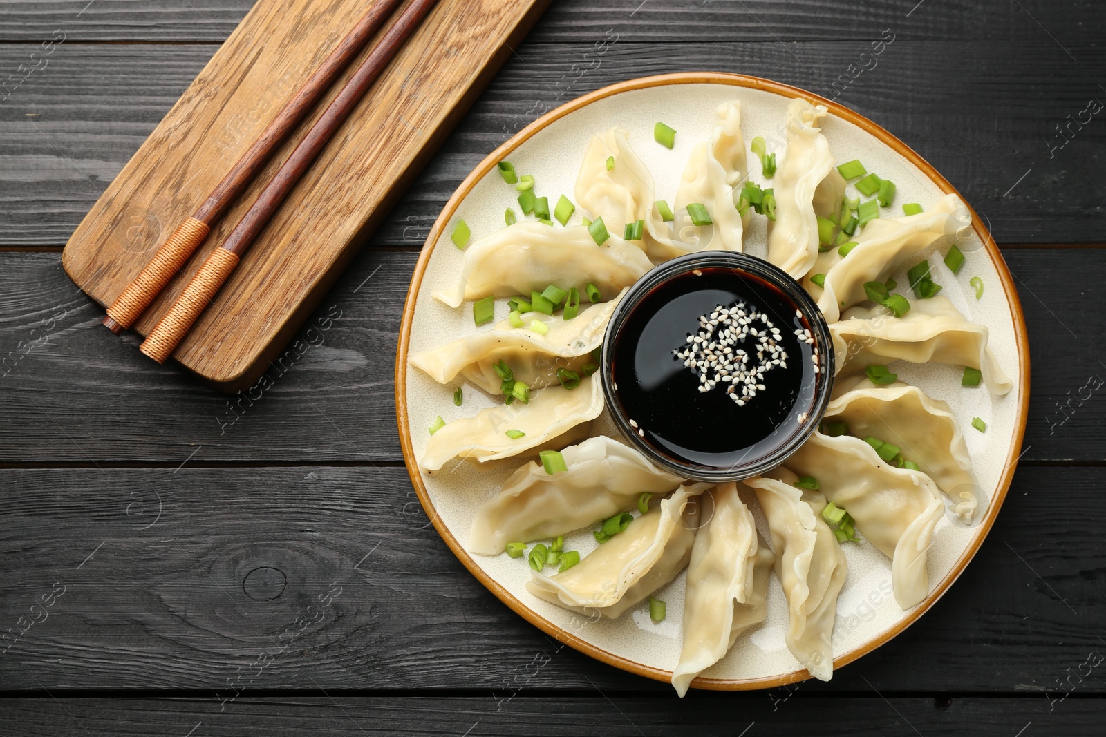 Photo of Tasty boiled gyoza (dumplings) with green onion served on black wooden table, flat lay