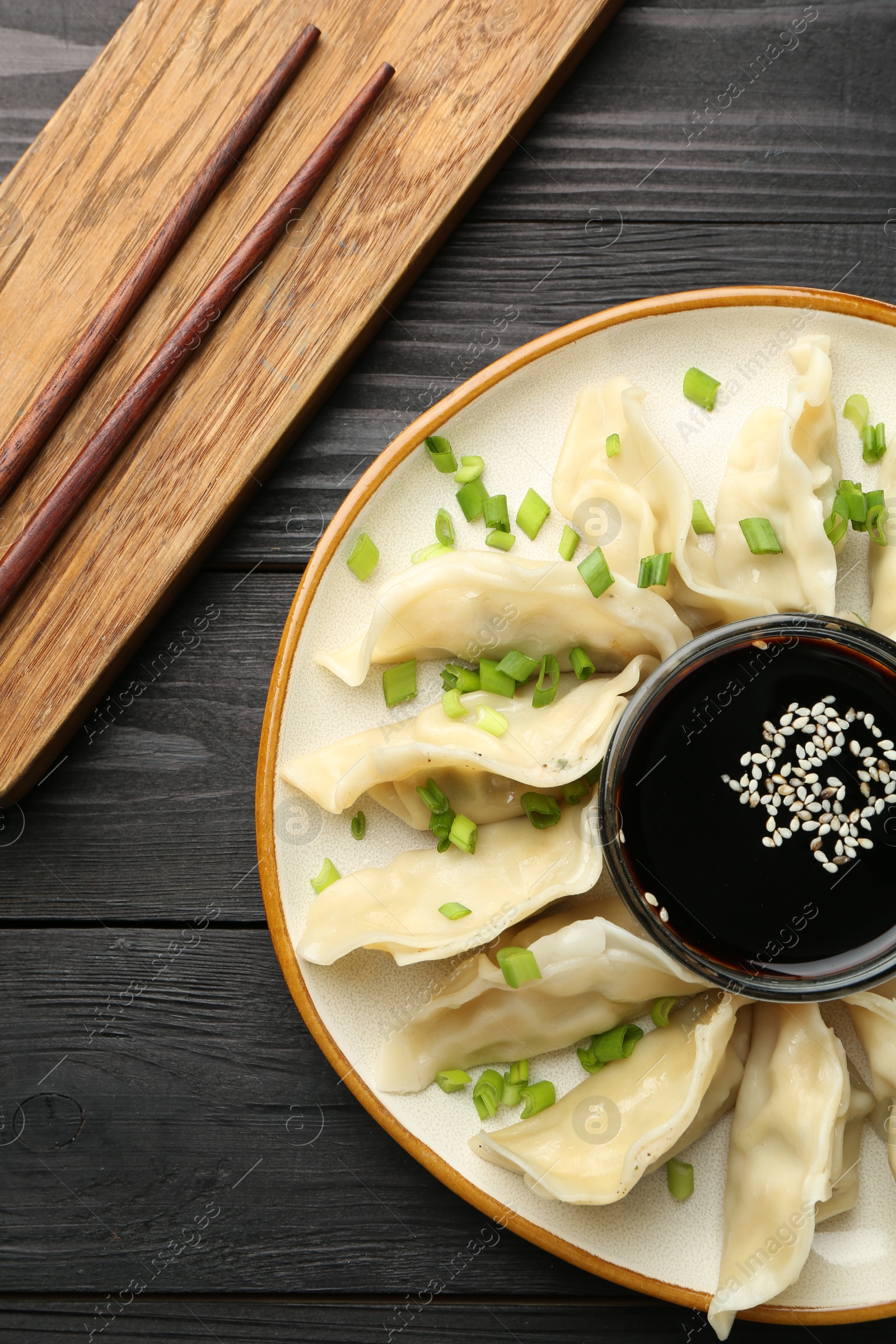 Photo of Tasty boiled gyoza (dumplings) with green onion served on black wooden table, flat lay