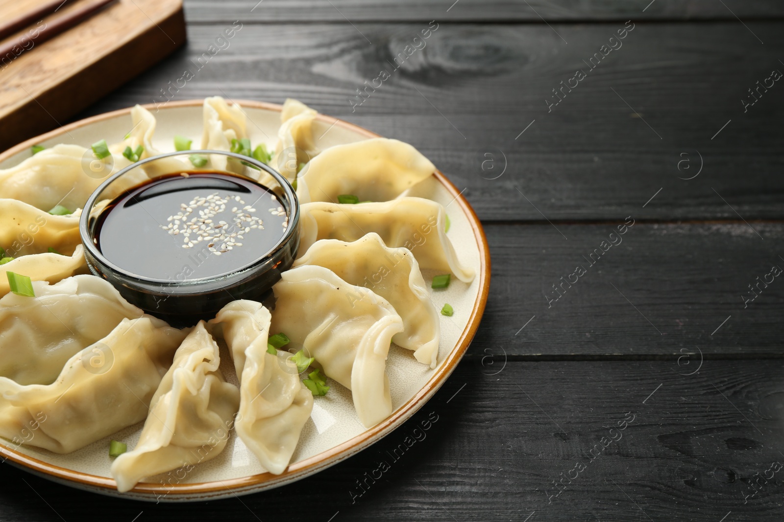 Photo of Tasty boiled gyoza (dumplings) with green onion served on black wooden table, closeup. Space for text