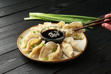 Photo of Woman taking tasty boiled gyoza (dumpling) with chopsticks at wooden table, closeup