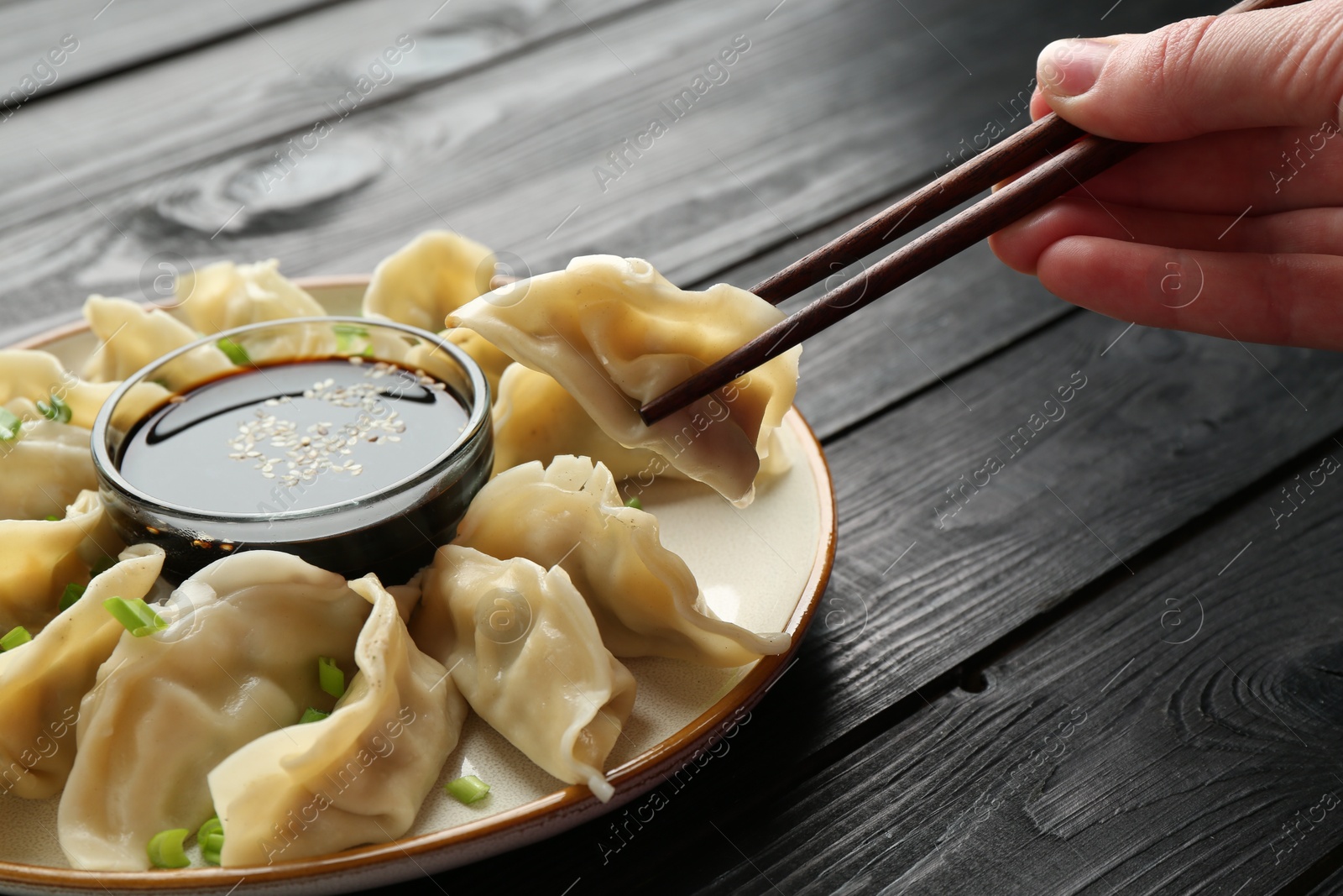 Photo of Woman taking tasty boiled gyoza (dumpling) with chopsticks at wooden table, closeup